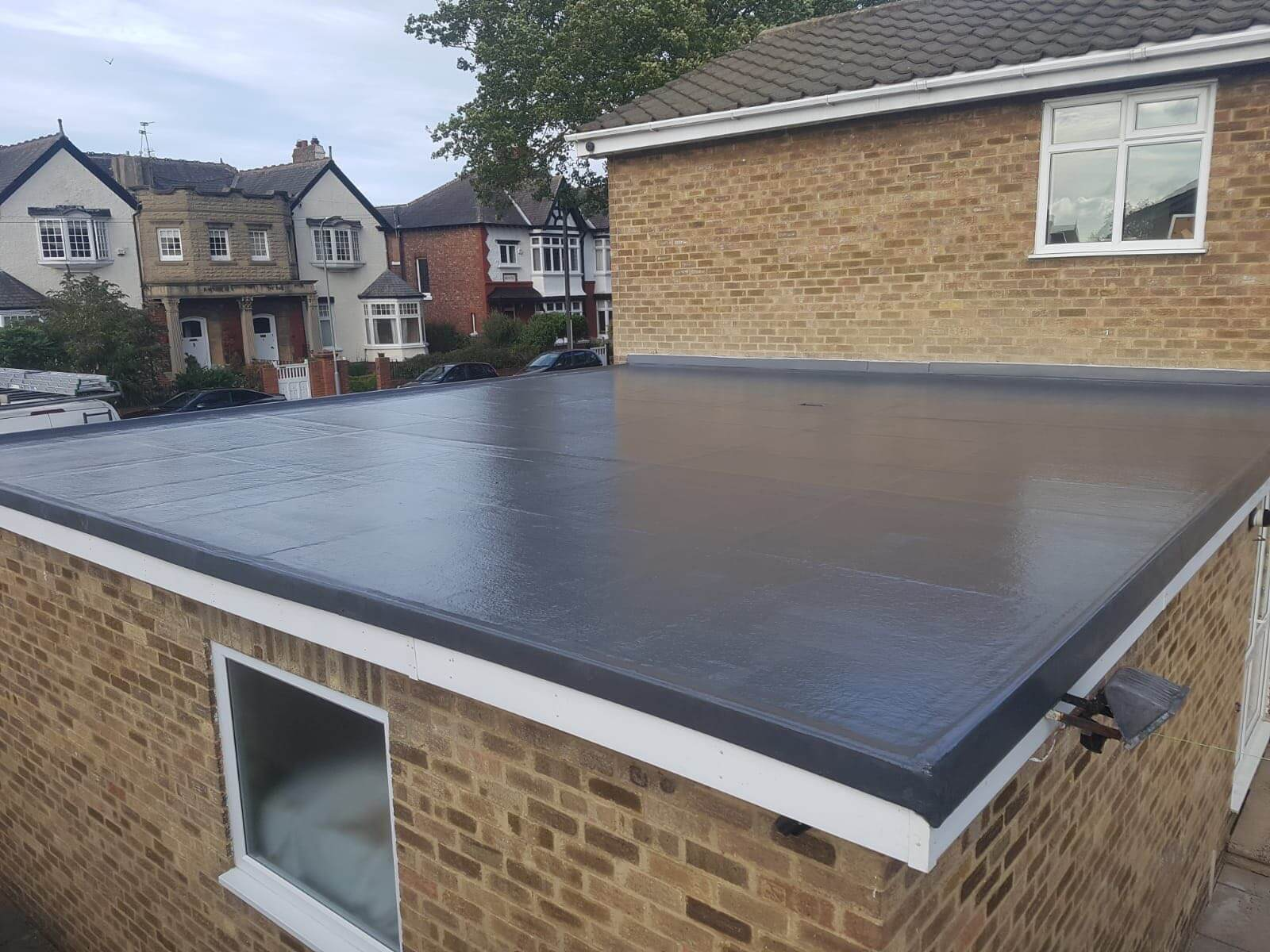Newly installed dark grey GRP fibreglass flat roof on a brick extension