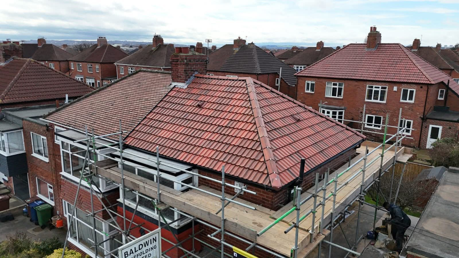 Newly completed hipped tile roof on a scaffolded semi-detached house during a full re-roof