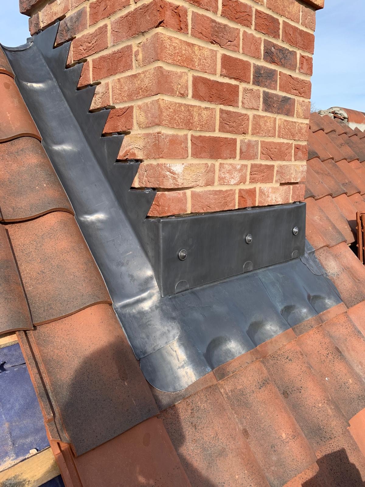New stepped lead flashing and soakers around a brick chimney on a tiled roof